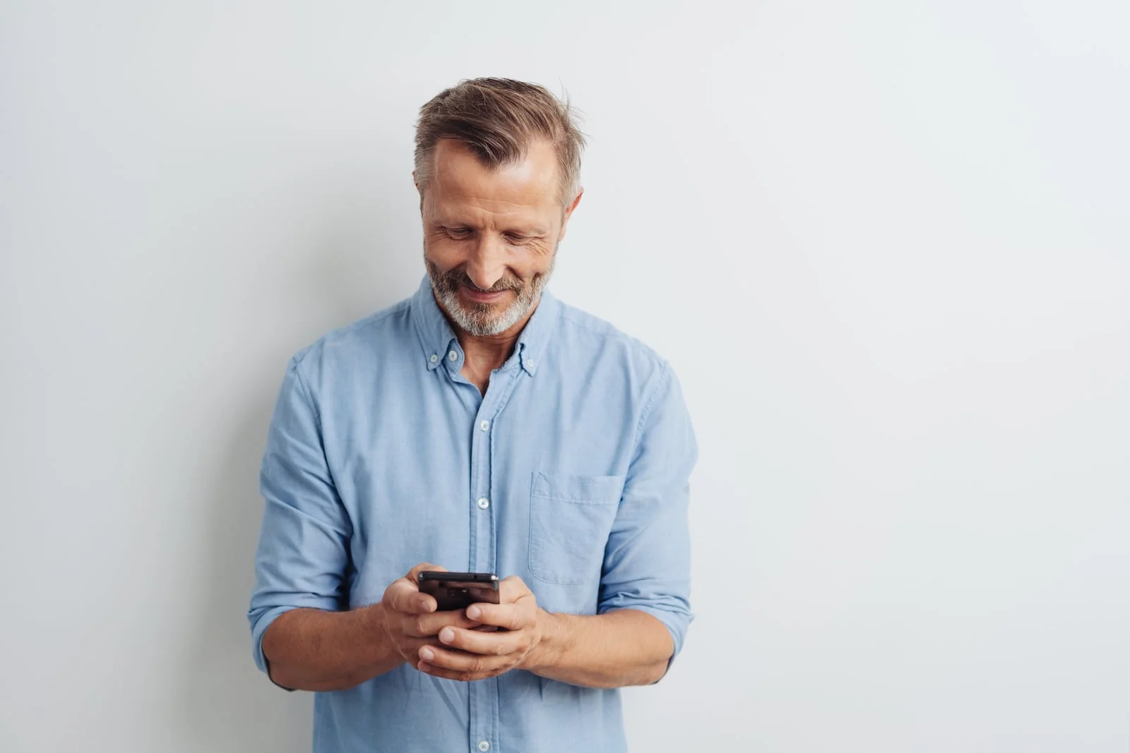 man looking down at his phone smiling